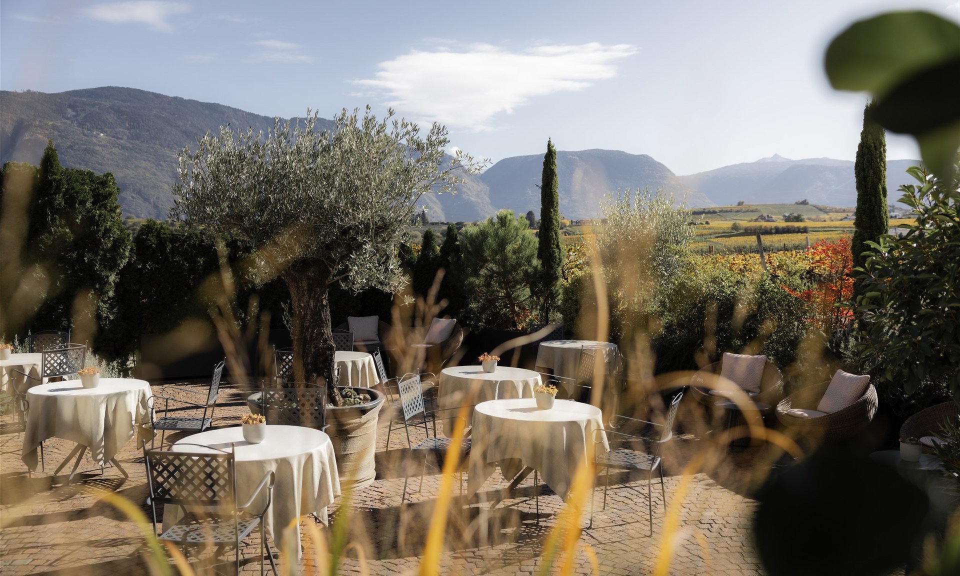 Terrazza soleggiata con tavoli e sedie davanti a montagne e vigneti