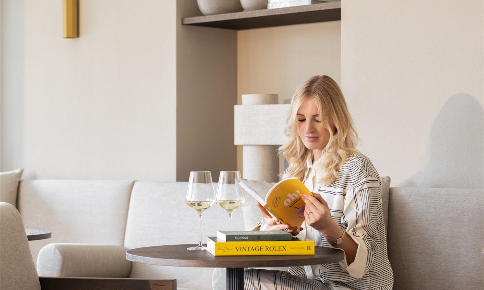 Donna che legge un libro al tavolo di un caffè con bicchieri di vino e libri accanto