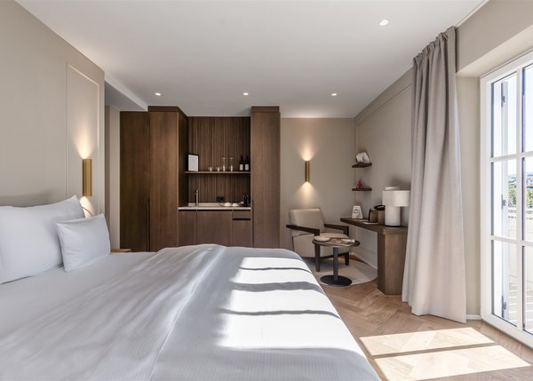 Lingers Junior Suites Helles Hotelzimmer mit großem Bett, Holzmöbeln und Zugang zum Balkon.