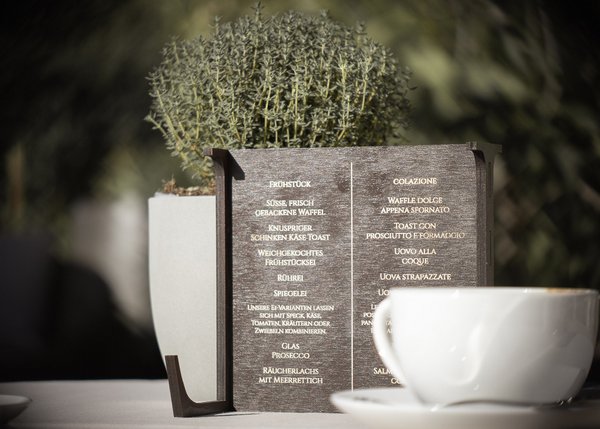 Frühstücksmenü auf Holztafel neben Pflanze und weißer Tasse auf Tisch