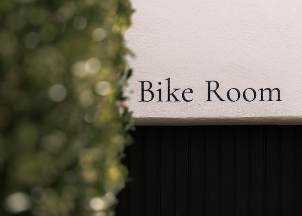 Schild mit der Aufschrift Bike Room an einer weißen Wand neben grünen Pflanzen