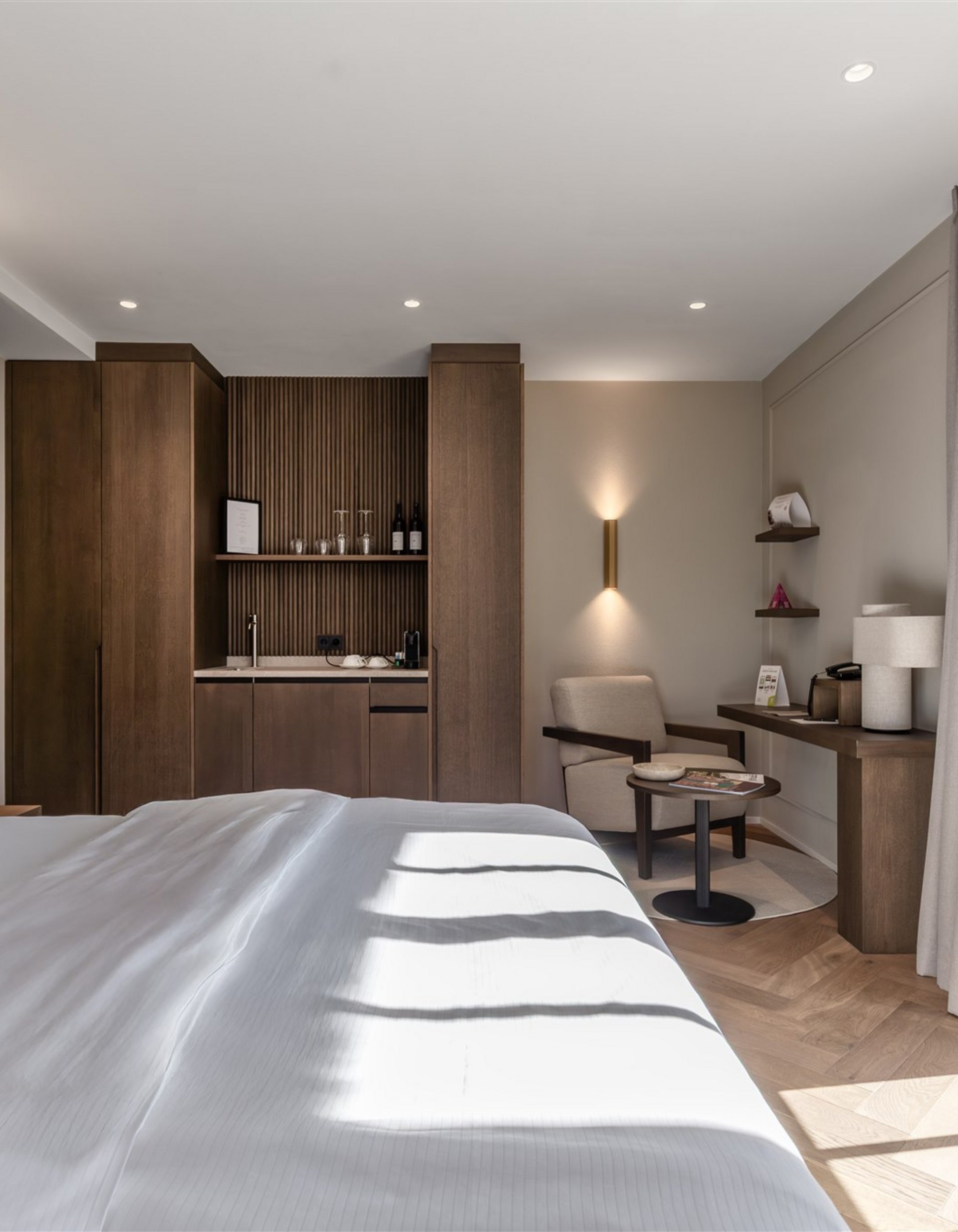 Camera d'hotel luminosa con letto grande, poltrona, scrivania e balcone