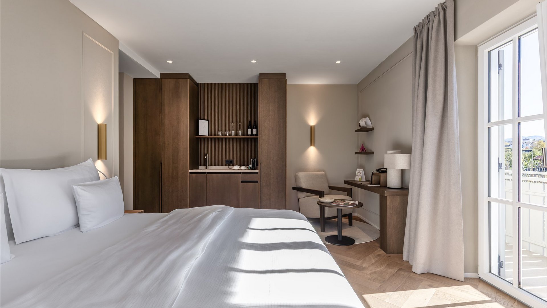 Helles Hotelzimmer mit großem Bett, Sessel, Schreibtisch und Balkon