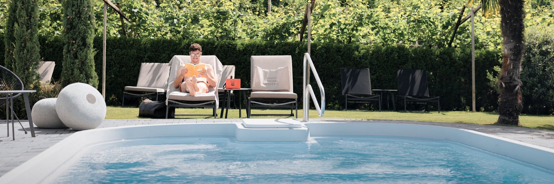 Mann liest am Pool auf einer Liege mit Blick auf grüne Weinberge