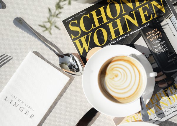 Frühstück mit Cappuccino, Croissants und Zeitschrift auf weißem Tisch