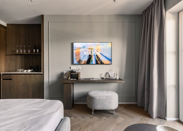 Lingers Junior Suites Modern eingerichtetes Hotelzimmer mit Schreibtisch, TV und Fenster mit Vorhängen