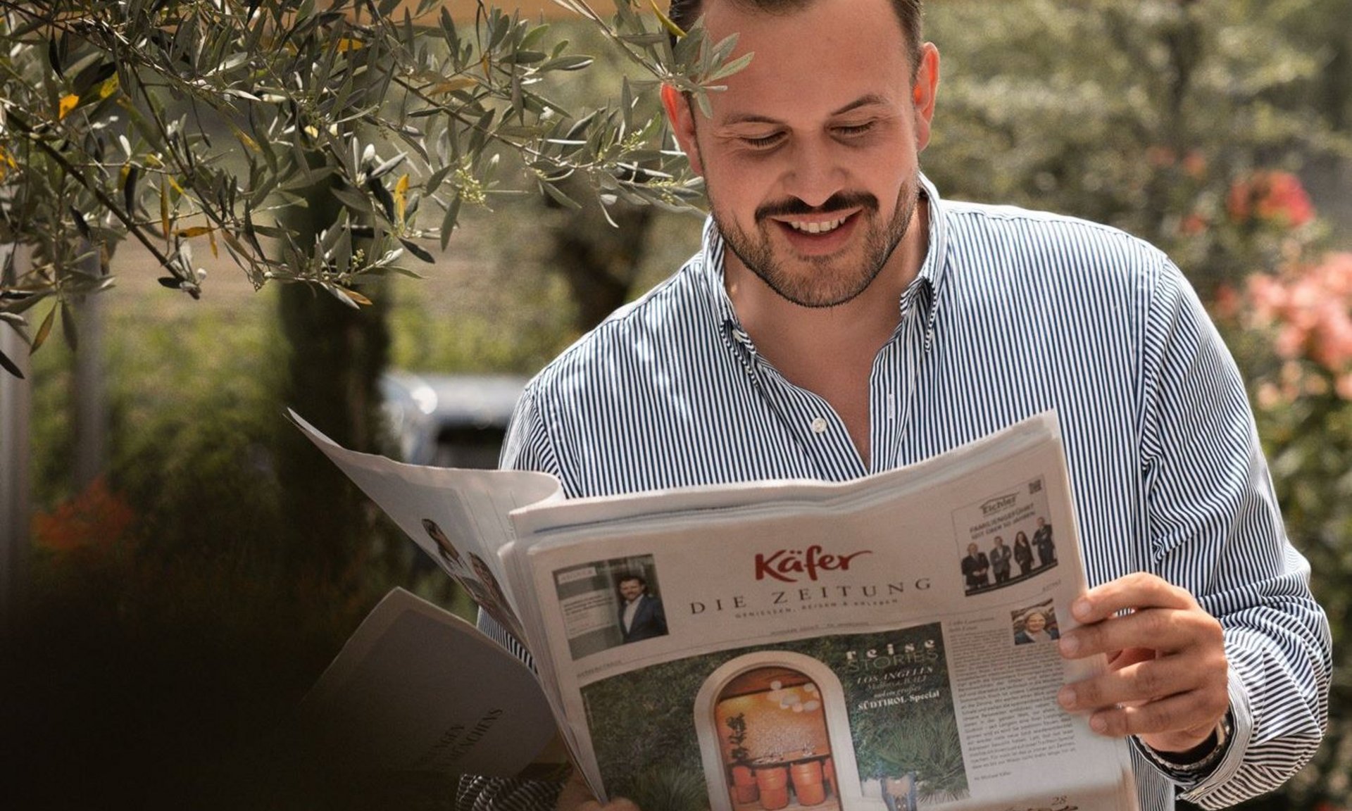 Gli scatti più belli del Lingers Uomo legge un giornale all'aperto sotto un ombrellone vicino a un ulivo