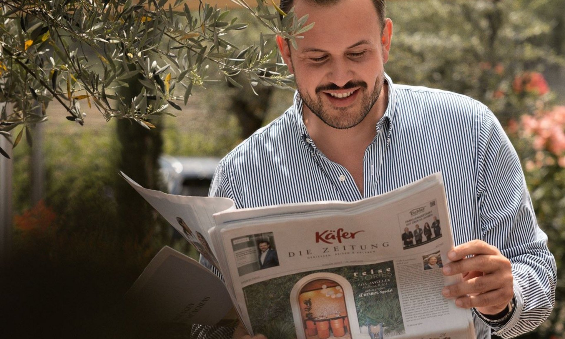 Lingers beste Schnappschüsse Mann liest Zeitung im Freien unter Sonnenschirm neben Olivenbaum