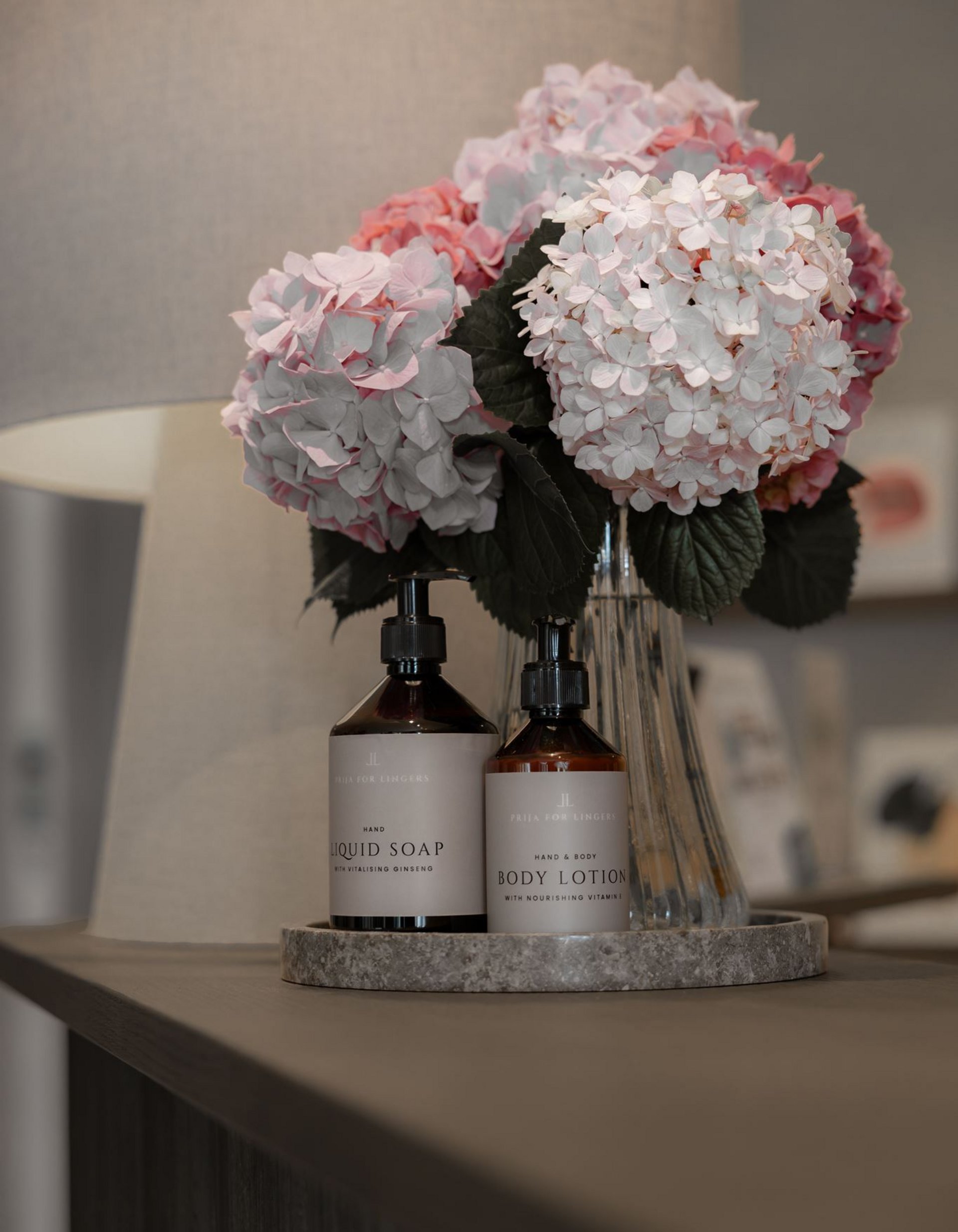 Bottles of liquid soap and body lotion next to a vase with pink hydrangeas